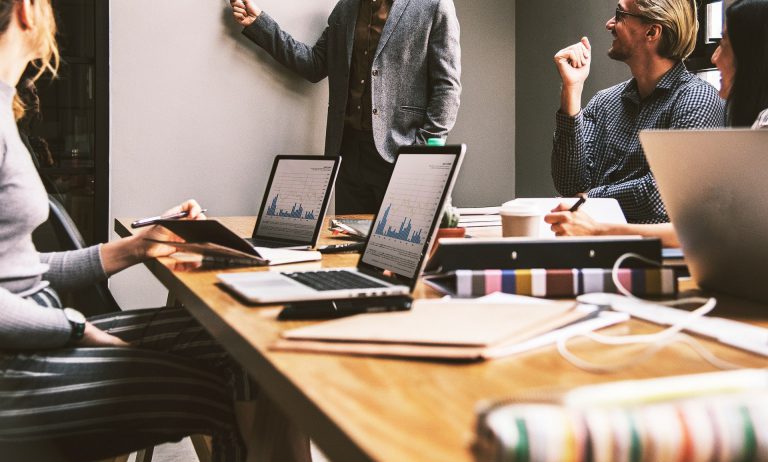 business meeting with men and women. one man is presenting while others are smiling and using their computers for not taking or following along