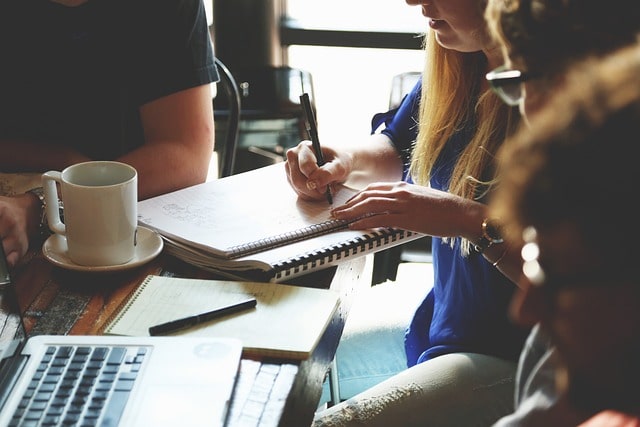 people at a meeting while a woman takes notes. Drinking coffee near a laptop